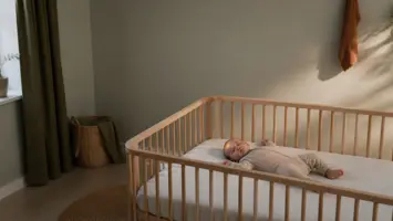 Baby sover sikkert på ryggen i en tom tremmeseng med fast lagen